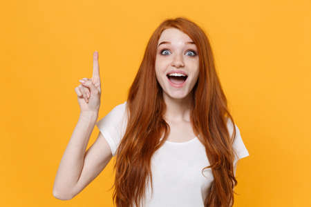 Excited young redhead woman girl in white blank empty t-shirt posing isolated on yellow background...