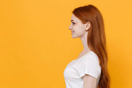 Side view of smiling young redhead woman girl in white blank empty t-shirt posing isolated on yellow background studio portrait. People emotions lifestyle concept. Mock up copy space. Looking aside.の写真素材
