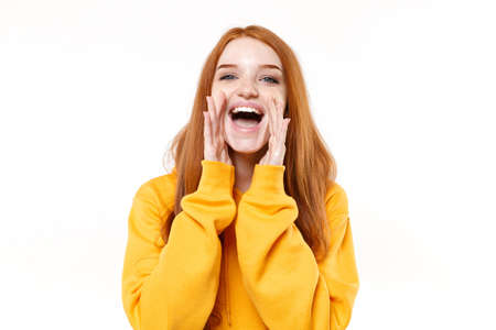 Cheerful young redhead woman girl in casual yellow hoodie posing isolated on white background studio portrait. People lifestyle concept. Mock up copy space. Screaming with hands gesture near mouth.の写真素材