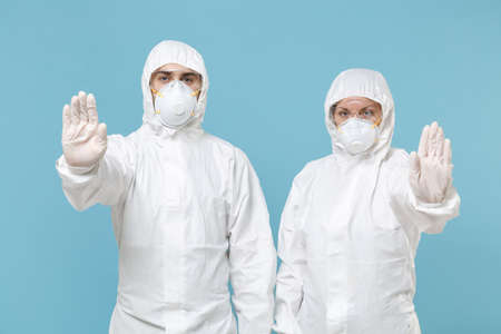 Two people in protective suits respirator masks isolated on blue background studio. Epidemic...