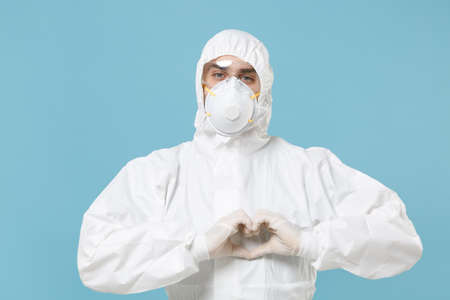 Man in white protective suit respirator mask isolated on blue background studio. Epidemic pandemic...