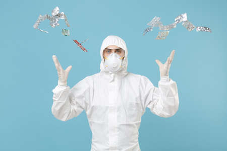 Man in white protective suit respirator mask throw out pack tablets pills drugs isolated on blue...