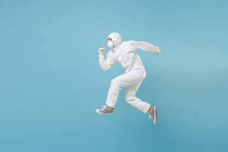 Man in white protective suit respirator mask run jump isolated on blue background studio. Epidemic...