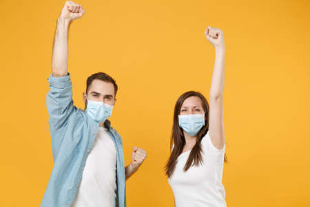 Two people in sterile face masks white t-shirts isolated on yellow background studio. Epidemic...
