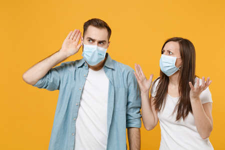 Two people in sterile face masks white t-shirts isolated on yellow background studio. Epidemic...