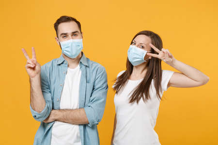 Two people in sterile face masks white t-shirts isolated on yellow background studio. Epidemic...