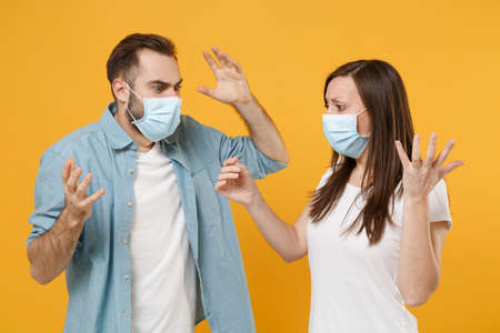 Two people in sterile face masks hold thermometer isolated on yellow background studio. Epidemic...
