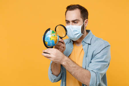 Young man in sterile face mask posing isolated on yellow wall background in studio. Epidemic...