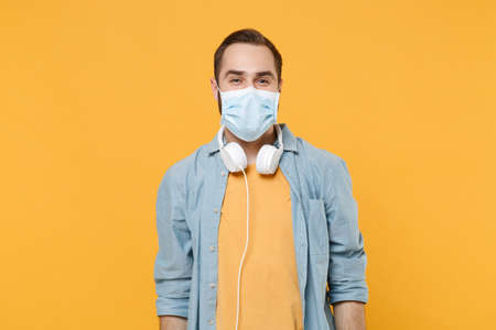 Cheerful young man in sterile face mask with headphones posing isolated on yellow background studio portrait. Epidemic pandemic rapidly spreading coronavirus 2019-ncov sars covid-19 flu virus concept.の写真素材