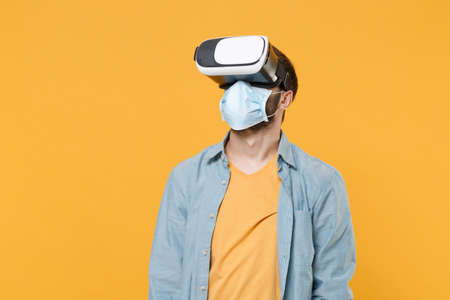 Young man in sterile face mask posing isolated on yellow wall background studio portrait. Epidemic...
