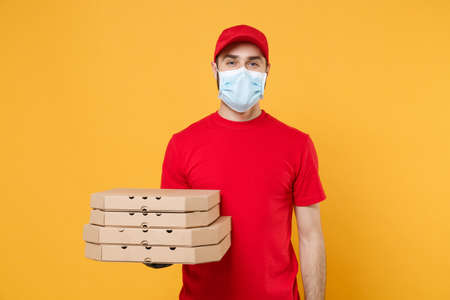 Delivery man employee in red cap blank t-shirt uniform mask gloves give food order pizza boxes isolated on yellow background studio. Service quarantine pandemic coronavirus virus flu 2019-ncov conceptの写真素材