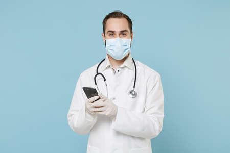 Male doctor man in medical gown sterile face mask gloves isolated on blue background. Epidemic...