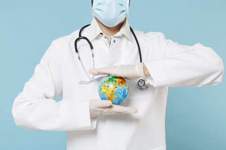 Cropped image of male doctor man in medical gown sterile face mask gloves isolated on blue background. Epidemic pandemic coronavirus 2019-ncov sars covid-19 flu virus concept. Hold Earth world globe.の写真素材