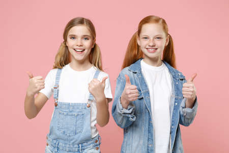 Cheerful little kids girls 12-13 years old in white t-shirt, denim clothes isolated on pastel pink background children portrait. Childhood lifestyle concept. Mock up copy space. Showing thumbs up.の写真素材