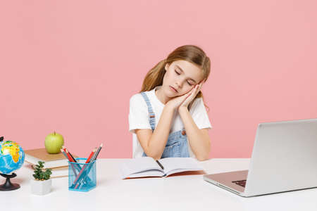Tired little kid schoolgirl 12-13 years old study at desk with laptop isolated on pink background. School distance education at home during quarantine concept. Sleeping with folded hands under cheek.の写真素材
