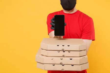 Delivery man employee in red cap blank t-shirt uniform mask gloves give food order pizza boxes isolated on yellow background studio. Service quarantine pandemic coronavirus virus flu 2019-ncov conceptの写真素材