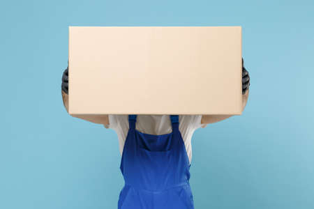 Delivery man in cap t-shirt uniform sterile face mask gloves isolated on blue background studio. Guy employee courier hold cardboard box Service quarantine coronavirus virus covid-19 2019-ncov conceptの写真素材