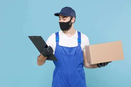 Delivery man in cap t-shirt uniform sterile face mask gloves isolated on blue background studio. Guy employee courier hold cardboard box Service quarantine coronavirus virus covid-19 2019-ncov conceptの写真素材
