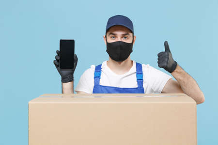 Delivery man in cap t-shirt uniform sterile face mask gloves isolated on blue background studio. Guy...