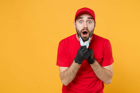 Delivery man in red cap blank t-shirt uniform sterile face mask gloves isolated on yellow background...