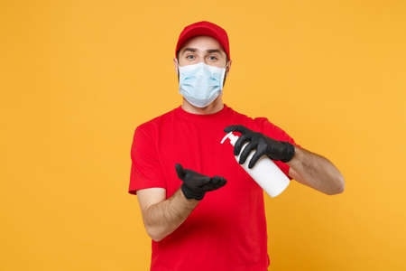 Delivery man employee in red cap t-shirt uniform sterile face mask glove hold bottle sanitizer soap isolated on yellow background studio Service quarantine pandemic coronavirus virus 2019-ncov conceptの写真素材