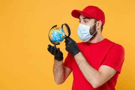 Delivery man in red cap blank t-shirt uniform sterile face mask gloves isolated on yellow background studio Guy employee working courier Service quarantine pandemic coronavirus virus 2019-ncov conceptの写真素材