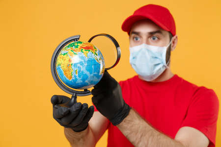 Delivery man in red cap blank t-shirt uniform sterile face mask gloves isolated on yellow background studio Guy employee working courier Service quarantine pandemic coronavirus virus 2019-ncov conceptの写真素材