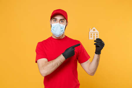 Delivery man in red cap blank t-shirt uniform sterile face mask gloves isolated on yellow background studio Guy employee working courier Service quarantine pandemic coronavirus virus 2019-ncov conceptの写真素材