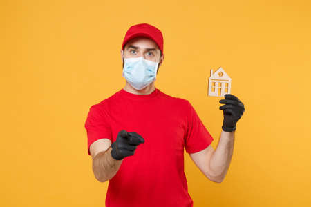 Delivery man in red cap blank t-shirt uniform sterile face mask gloves isolated on yellow background studio Guy employee working courier Service quarantine pandemic coronavirus virus 2019-ncov conceptの写真素材