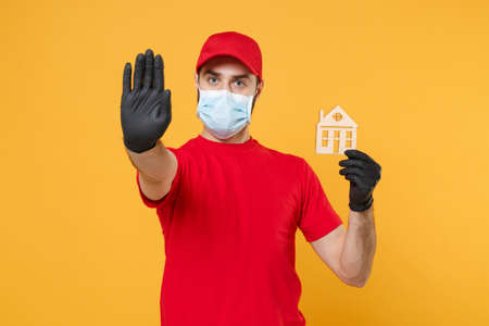 Delivery man in red cap blank t-shirt uniform sterile face mask gloves isolated on yellow background studio Guy employee working courier Service quarantine pandemic coronavirus virus 2019-ncov conceptの写真素材