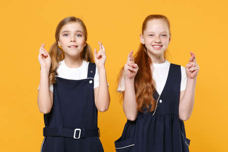 Two young little girls 12-13 years old in white t-shirt blue school uniform dresses isolated on yellow background children studio portrait Childhood kids education lifestyle concept Mock up copy spaceの写真素材