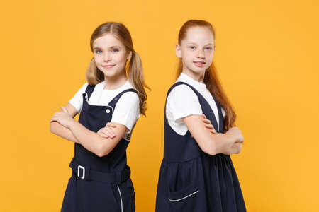 Two young little girls 12-13 years old in white t-shirt blue school uniform dresses isolated on yellow background children studio portrait Childhood kids education lifestyle concept Mock up copy spaceの写真素材