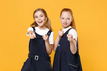 Two young little girls 12-13 years old in white t-shirt blue school uniform dresses isolated on yellow background children studio portrait Childhood kids education lifestyle concept Mock up copy spaceの写真素材