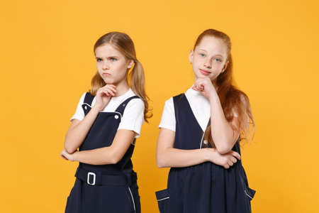 Two young little girls 12-13 years old in white t-shirt blue school uniform dresses isolated on yellow background children studio portrait Childhood kids education lifestyle concept Mock up copy spaceの写真素材