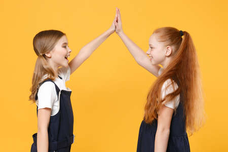 Two young little girls 12-13 years old in white t-shirt blue school uniform dresses isolated on yellow background children studio portrait Childhood kids education lifestyle concept Mock up copy spaceの写真素材