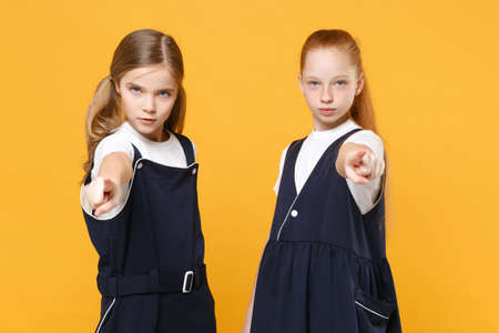 Two young little girls 12-13 years old in white t-shirt blue school uniform dresses isolated on yellow background children studio portrait Childhood kids education lifestyle concept Mock up copy spaceの写真素材