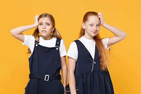 Two young little girls 12-13 years old in white t-shirt blue school uniform dresses isolated on yellow background children studio portrait Childhood kids education lifestyle concept Mock up copy spaceの写真素材