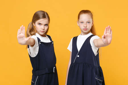 Two young little girls 12-13 years old in white t-shirt blue school uniform dresses isolated on yellow background children studio portrait Childhood kids education lifestyle concept Mock up copy spaceの写真素材