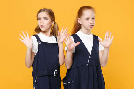 Two young little girls 12-13 years old in white t-shirt blue school uniform dresses isolated on yellow background children studio portrait Childhood kids education lifestyle concept Mock up copy spaceの写真素材