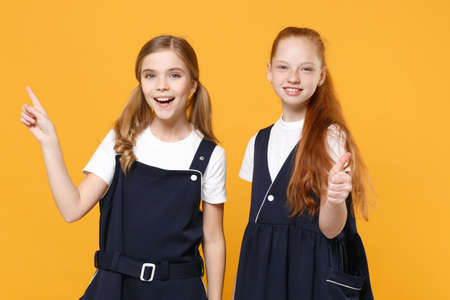 Two young little girls 12-13 years old in white t-shirt blue school uniform dresses isolated on yellow background children studio portrait Childhood kids education lifestyle concept Mock up copy spaceの写真素材