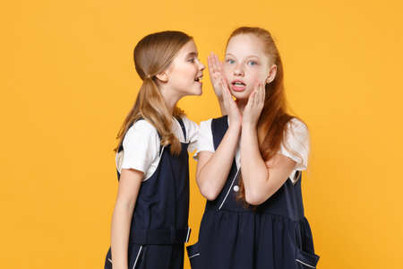 Two young little girls 12-13 years old in white t-shirt blue school uniform dresses isolated on yellow background children studio portrait Childhood kids education lifestyle concept Mock up copy spaceの写真素材