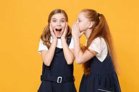 Two young little girls 12-13 years old in white t-shirt blue school uniform dresses isolated on yellow background children studio portrait Childhood kids education lifestyle concept Mock up copy spaceの写真素材