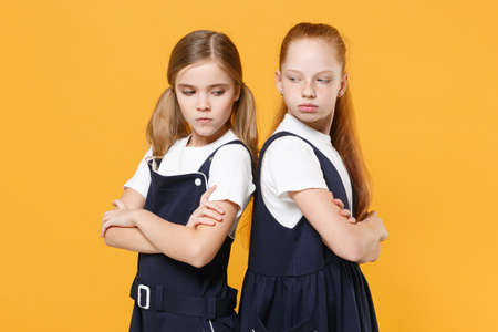 Two young little girls 12-13 years old in white t-shirt blue school uniform dresses isolated on yellow background children studio portrait Childhood kids education lifestyle concept Mock up copy spaceの写真素材