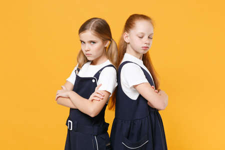 Two young little girls 12-13 years old in white t-shirt blue school uniform dresses isolated on yellow background children studio portrait Childhood kids education lifestyle concept Mock up copy spaceの写真素材