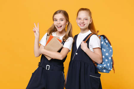 Girls 12-13 years old in white t-shirt blue school uniform dresses hold schoolbooks isolated on yellow background children studio portrait Childhood kids education lifestyle concept Mock up copy spaceの写真素材