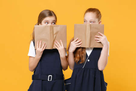 Girls 12-13 years old in white t-shirt blue school uniform dresses hold schoolbooks isolated on yellow background children studio portrait Childhood kids education lifestyle concept Mock up copy spaceの写真素材