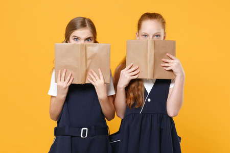 Girls 12-13 years old in white t-shirt blue school uniform dresses hold schoolbooks isolated on yellow background children studio portrait Childhood kids education lifestyle concept Mock up copy spaceの写真素材