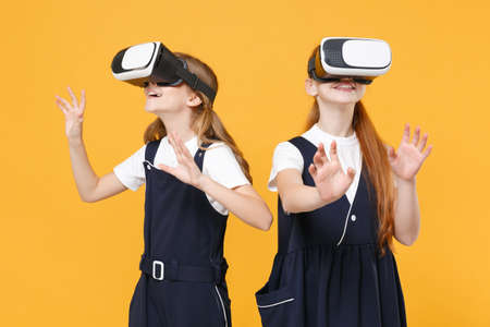Two girls 12-13 years old in headset virtual vr reality t-shirt blue school uniform isolated on yellow background children studio portrait Childhood kids education lifestyle concept Mock up copy spaceの写真素材