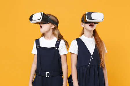 Two girls 12-13 years old in headset virtual vr reality t-shirt blue school uniform isolated on yellow background children studio portrait Childhood kids education lifestyle concept Mock up copy spaceの写真素材