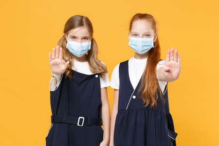 Two girls 12-13 years old in white t-shirt school uniform dresses sterile face mask isolated on yellow background children studio portrait Childhood kids education covid-19 concept Mock up copy spaceの写真素材